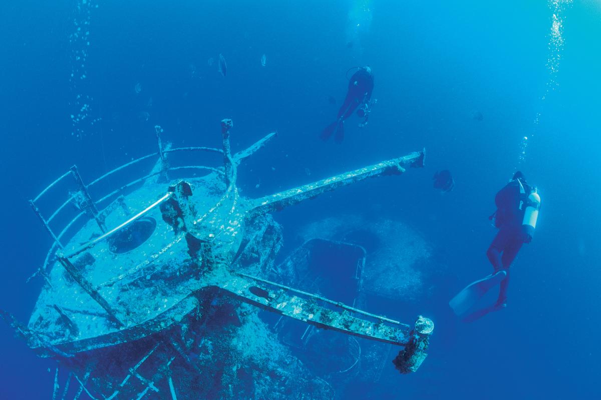 Scuba divers underwater near a sunken ship